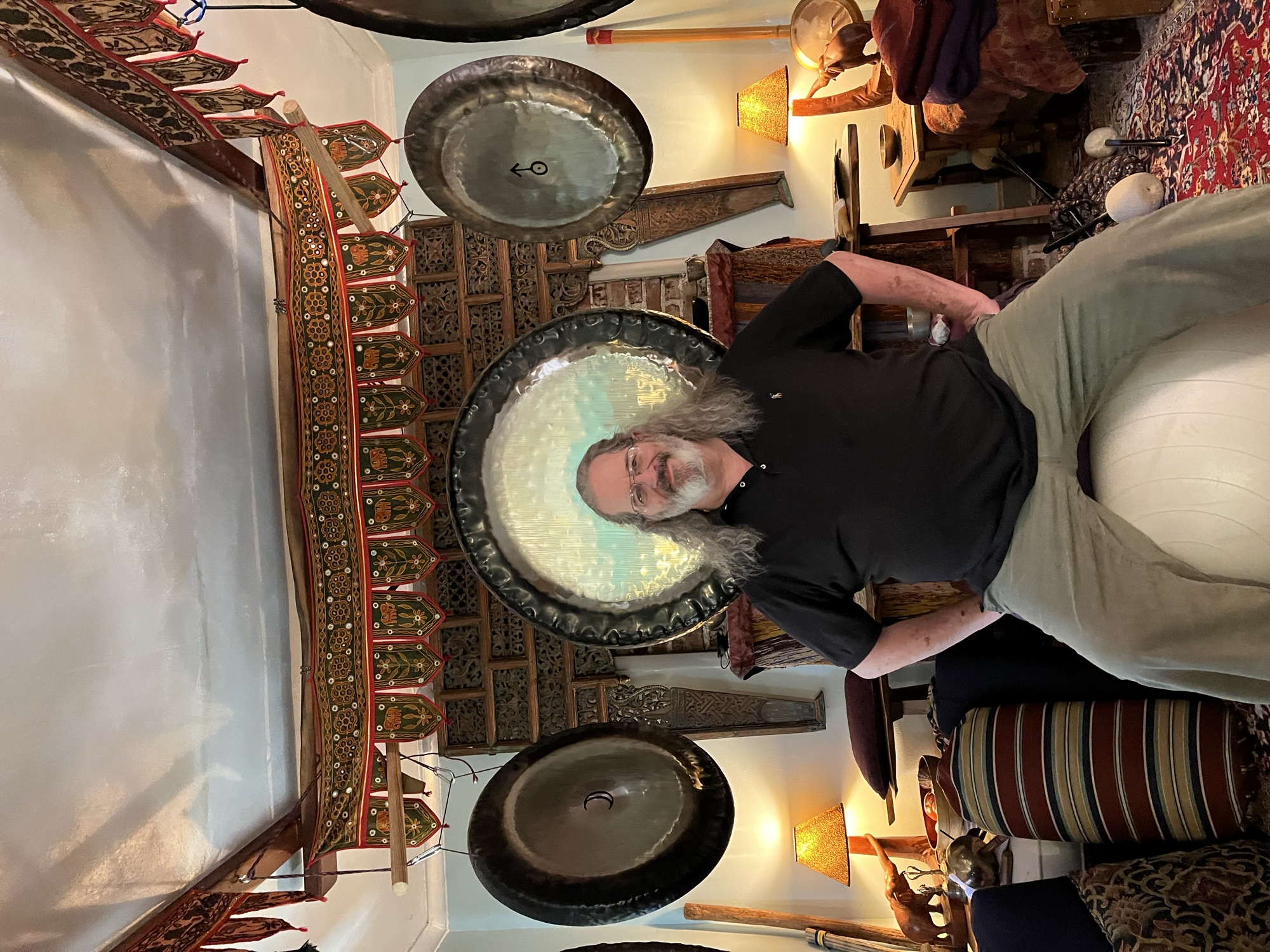 Lee Veal seated in his gong room, a great gong glowing behind him